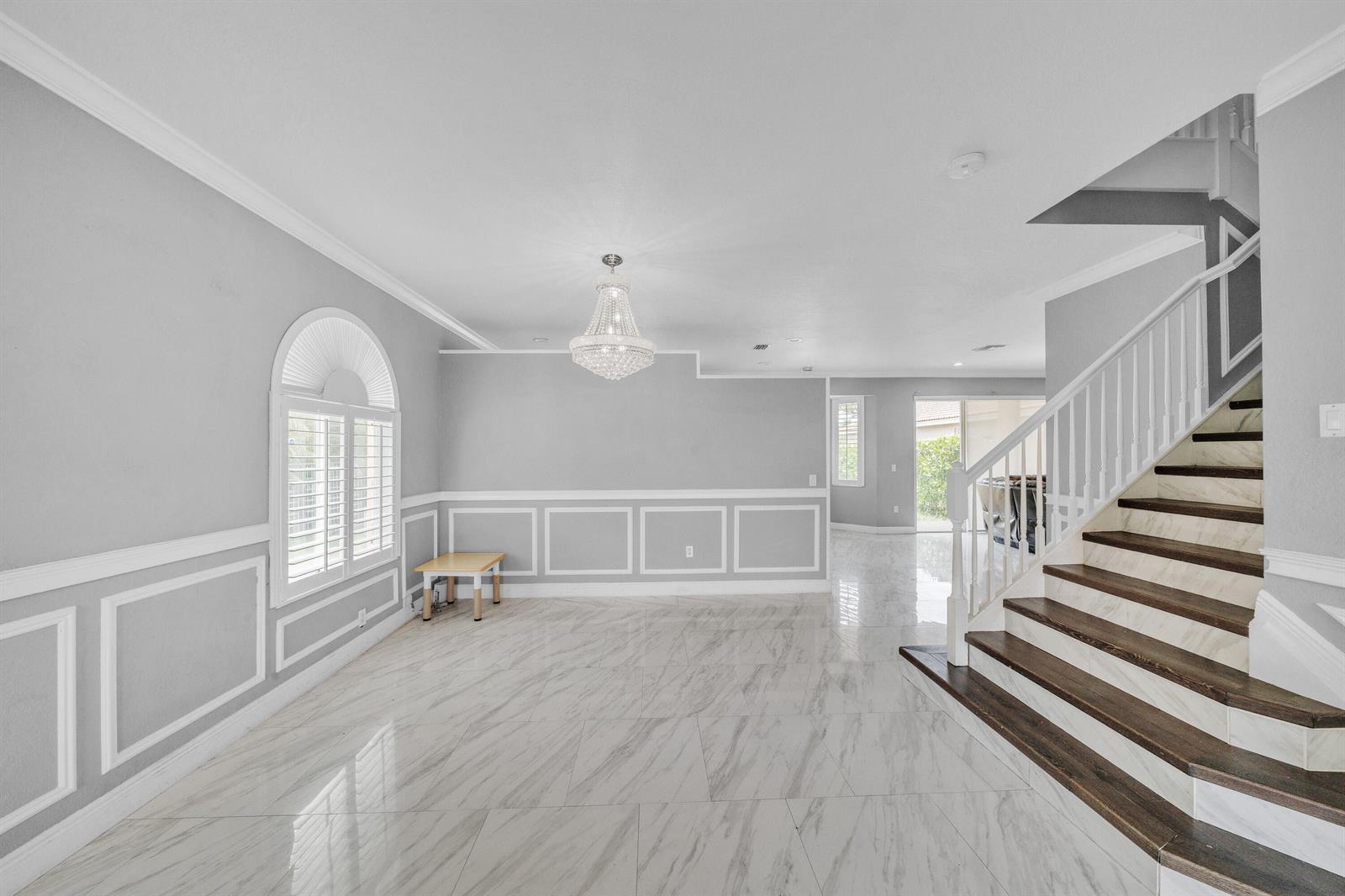 A bright foyer features marble-look tile flooring, a crystal chandelier, and a wooden staircase — 149 Bellezza Terrace, Royal Palm Beach FL 33411, ROYAL PALM BEACH, FL