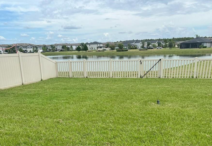 A grassy backyard features a white vinyl fence overlooking a pond and residential homes — 8403 CAPSTONE RANCH DRIVE, NEW PORT RICHEY, FL