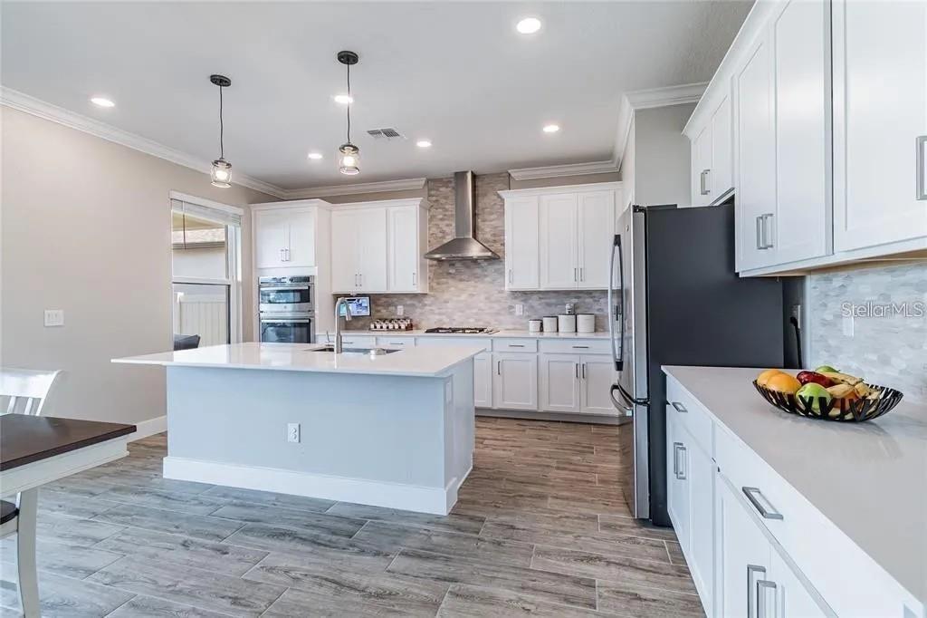 A modern kitchen features white cabinets, a large island with a sink, and stainless appliances — 8403 CAPSTONE RANCH DRIVE, NEW PORT RICHEY, FL
