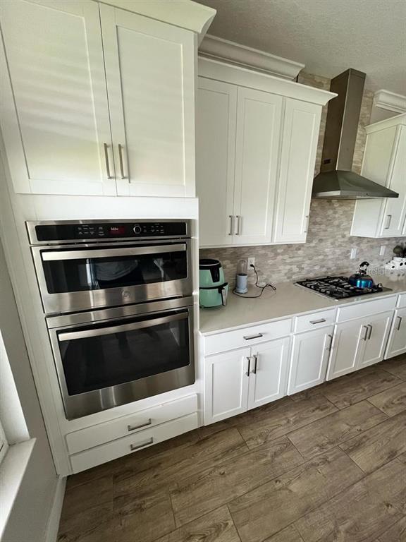 A kitchen features white cabinets, stainless steel double ovens, a range hood, and tile flooring — 8403 CAPSTONE RANCH DRIVE, NEW PORT RICHEY, FL