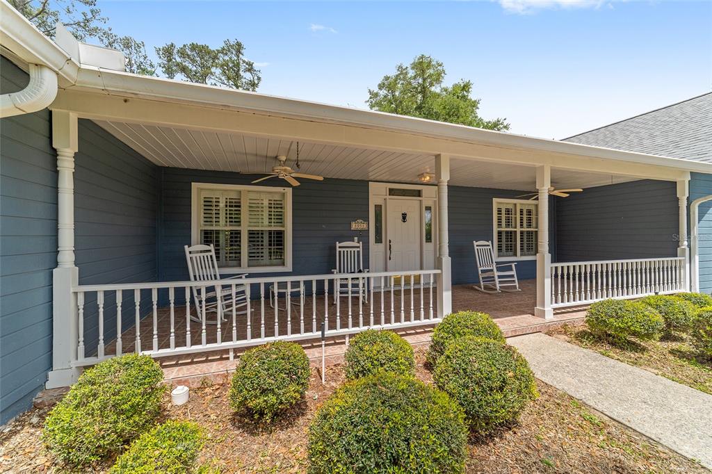 A covered front porch features white railings, rocking chairs, and blue siding on a house — 8051 NW 43RD LANE, OCALA, FL