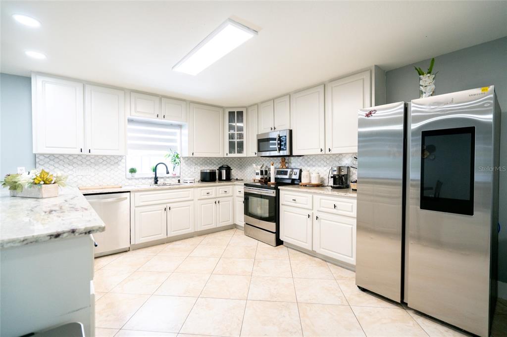A kitchen features white cabinets, granite countertops, stainless steel appliances, and light-colored tile flooring — 3615 MARCO DRIVE, TAMPA, FL