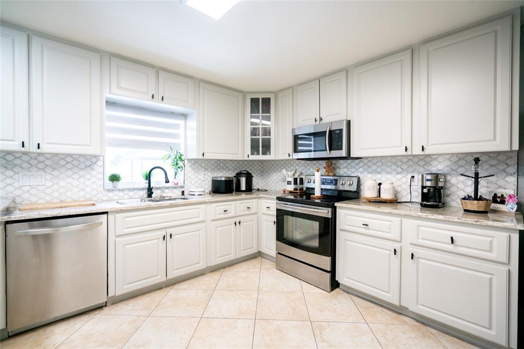 A kitchen with white cabinets, stainless steel appliances, granite countertops, and a patterned tile backsplash — 3615 MARCO DRIVE, TAMPA, FL
