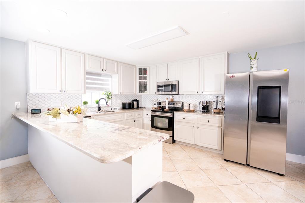 A kitchen features white cabinets, granite countertops, stainless steel appliances, and light-colored tile flooring — 3615 MARCO DRIVE, TAMPA, FL