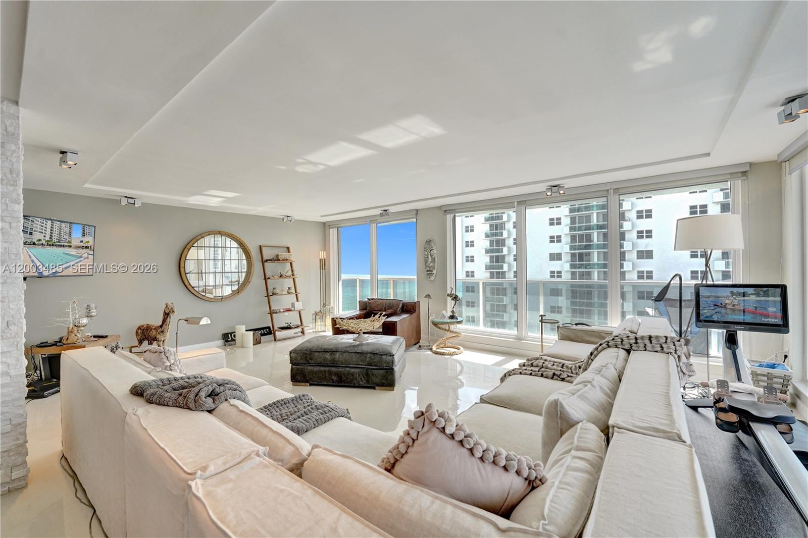 A bright living room features a large sectional sofa, leather ottoman, and floor-to-ceiling windows — 2751 S Ocean Dr # 908S, Hollywood FL 33019, HOLLYWOOD, FL