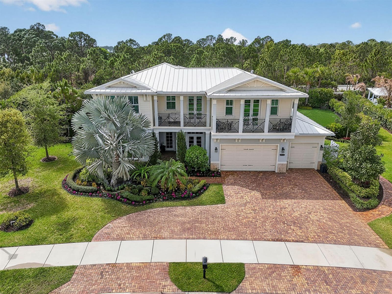 A two-story house with a metal roof, balconies, and a brick driveway sits on a lawn — 19966 SE Gallberry Drive, Jupiter FL 33458, JUPITER, FL