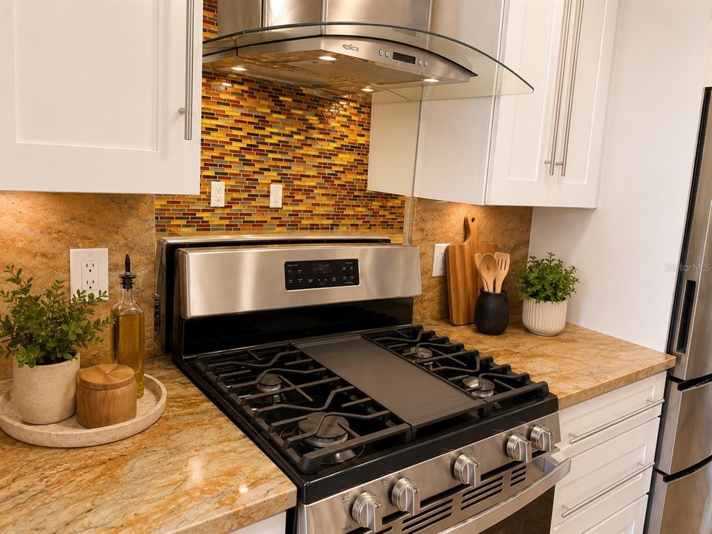 A kitchen features a stainless steel gas range, a glass range hood, and mosaic tile backsplash — 3128 59TH STREET S UNIT 109, GULFPORT, FL