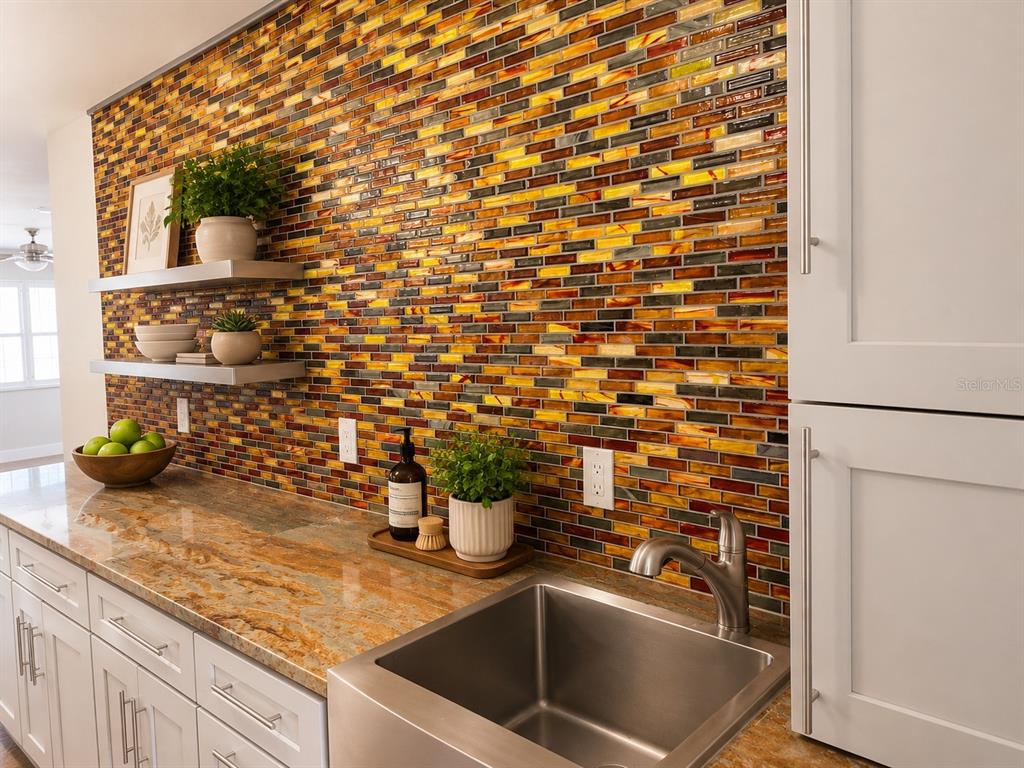 A kitchen features a multi-colored glass tile backsplash, granite countertops, and a stainless steel sink — 3128 59TH STREET S UNIT 109, GULFPORT, FL