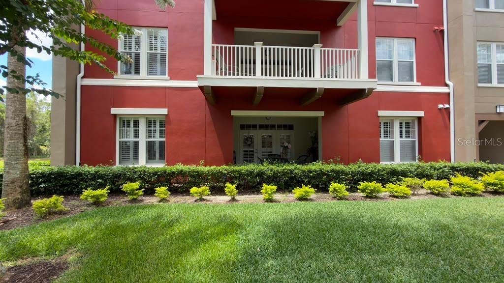 A red multi-story apartment building features a second-floor balcony and a ground-level patio — 1400 CELEBRATION AVENUE UNIT 105, CELEBRATION, FL