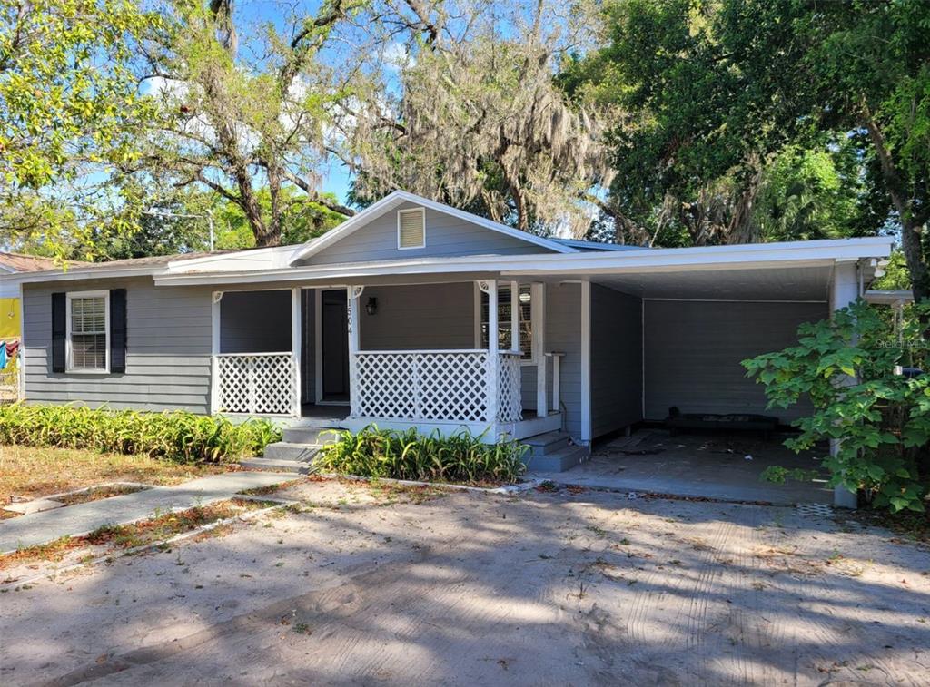 A gray single-story house with a front porch, lattice railing, and an attached carport — 1504 E 99TH AVENUE UNIT A, TAMPA, FL
