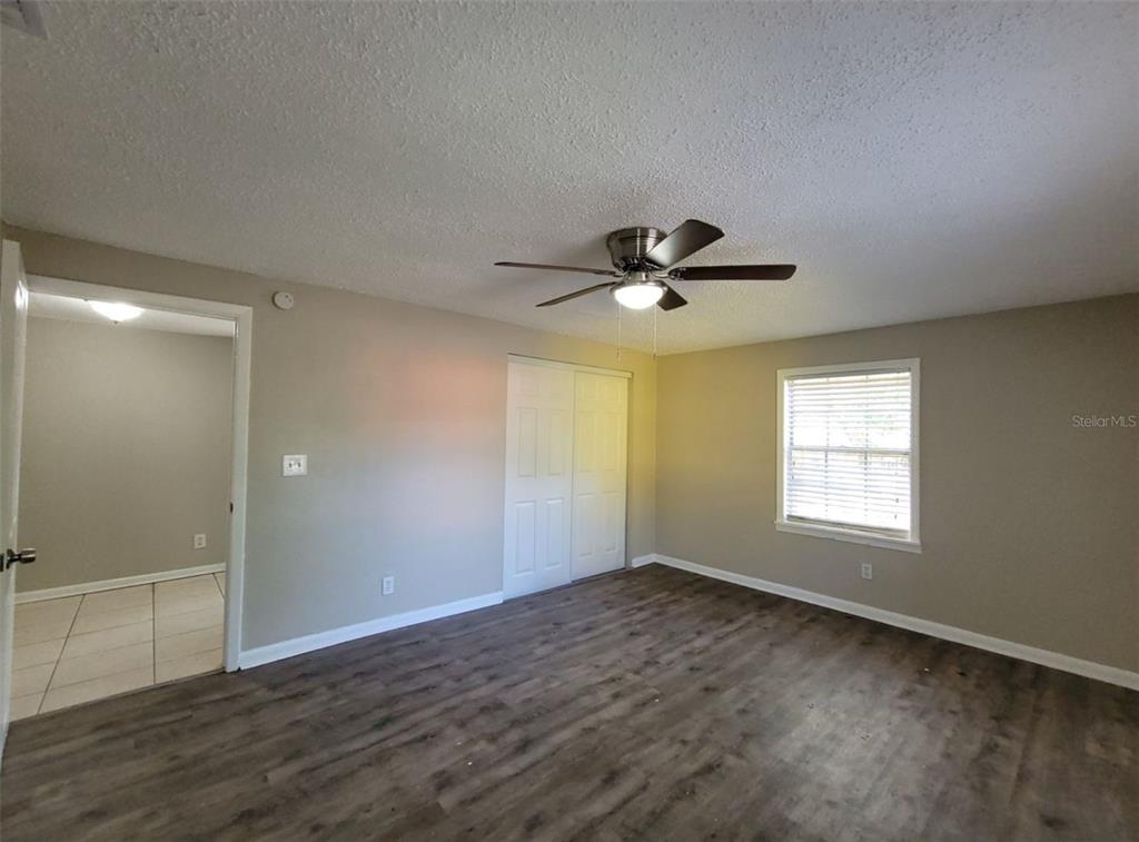 A bedroom with wood-look flooring, a ceiling fan, a closet, and a doorway to another room — 1504 E 99TH AVENUE UNIT A, TAMPA, FL