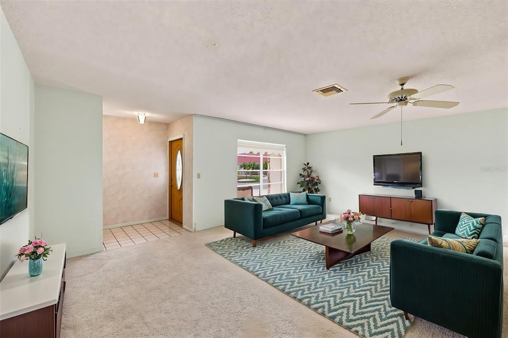 A living room features two teal sofas, a patterned rug, and a wooden media console — 127 WINTERSONG LANE, SUN CITY CENTER, FL