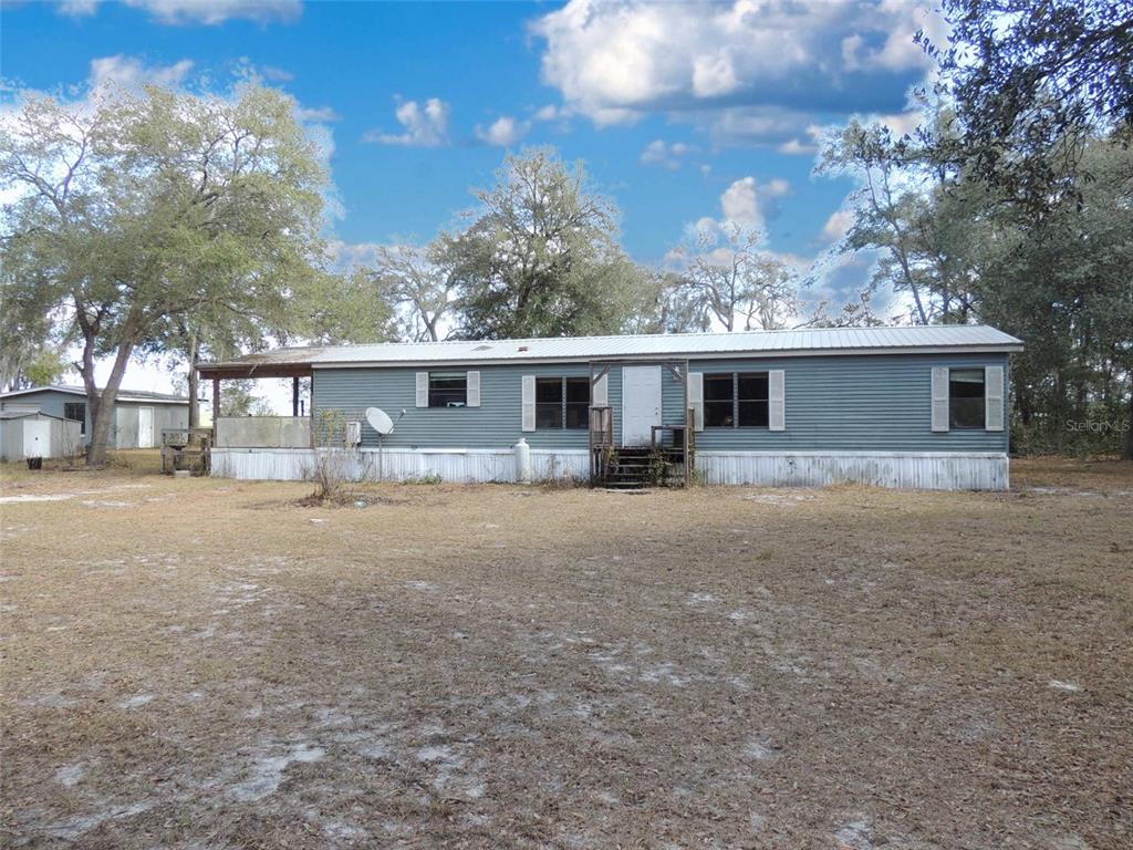 A single-story manufactured home with grey siding sits on a large, grassy lot — 4551 SE 138TH TERRACE, MORRISTON, FL