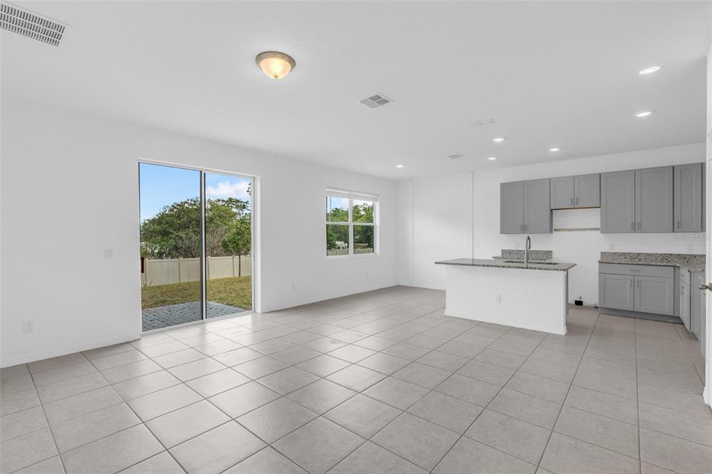 An open-concept kitchen and living area with gray cabinets, granite countertops, and tile flooring — 663 FAIRVIEW AVENUE, HAINES CITY, FL