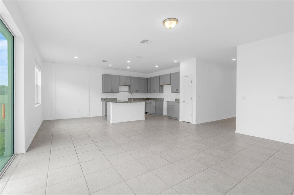An open-concept kitchen features gray cabinets, a granite island, and light tile flooring — 663 FAIRVIEW AVENUE, HAINES CITY, FL