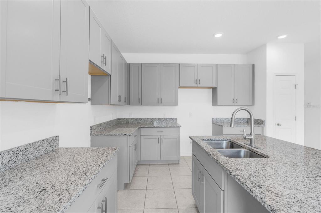 A kitchen features gray shaker cabinets, granite countertops, an island with a sink, and tile flooring — 663 FAIRVIEW AVENUE, HAINES CITY, FL