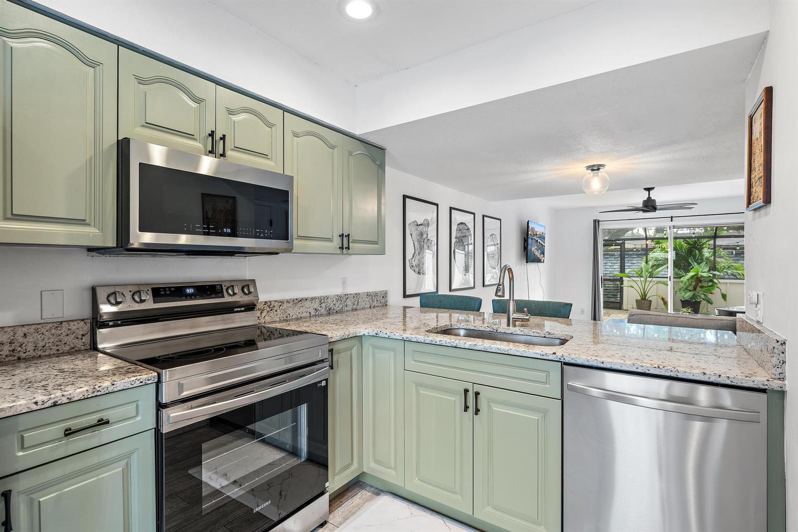 A kitchen features sage green cabinets, granite countertops, stainless steel appliances, and a breakfast bar — 6158 Riverwalk Lane # 6, Jupiter FL 33458, JUPITER, FL