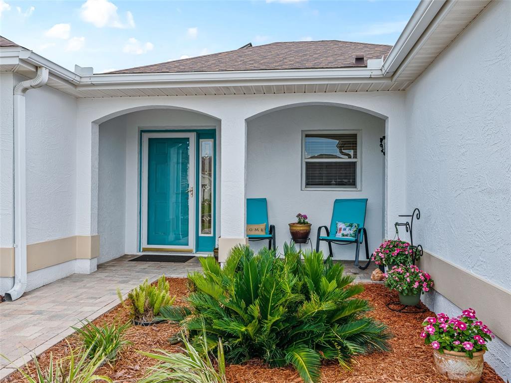 A single-story house with a white stucco exterior, a teal front door, and a paver walkway — 2121 GERARDO AVENUE, THE VILLAGES, FL