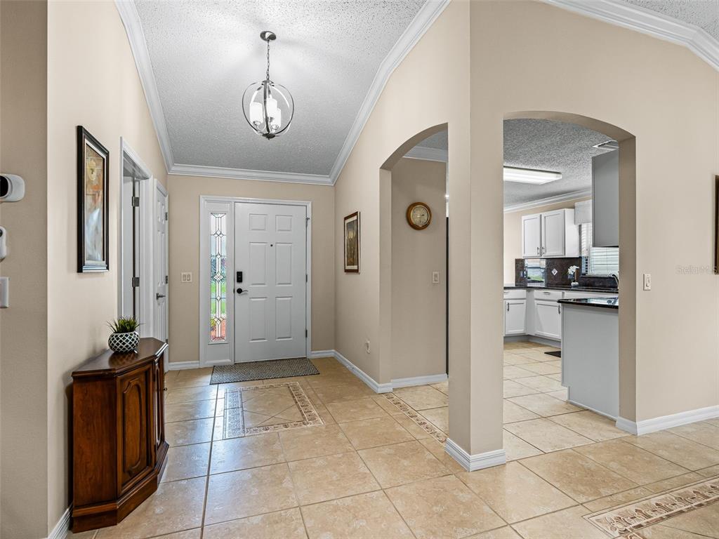 A view from an open blue front door into a tiled foyer with a chandelier — 2121 GERARDO AVENUE, THE VILLAGES, FL