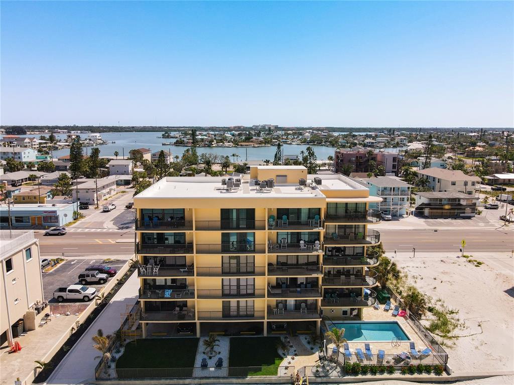 An aerial view of a multi-story yellow apartment building with balconies, a pool, and parking — 14146 GULF BOULEVARD UNIT 3A, MADEIRA BEACH, FL
