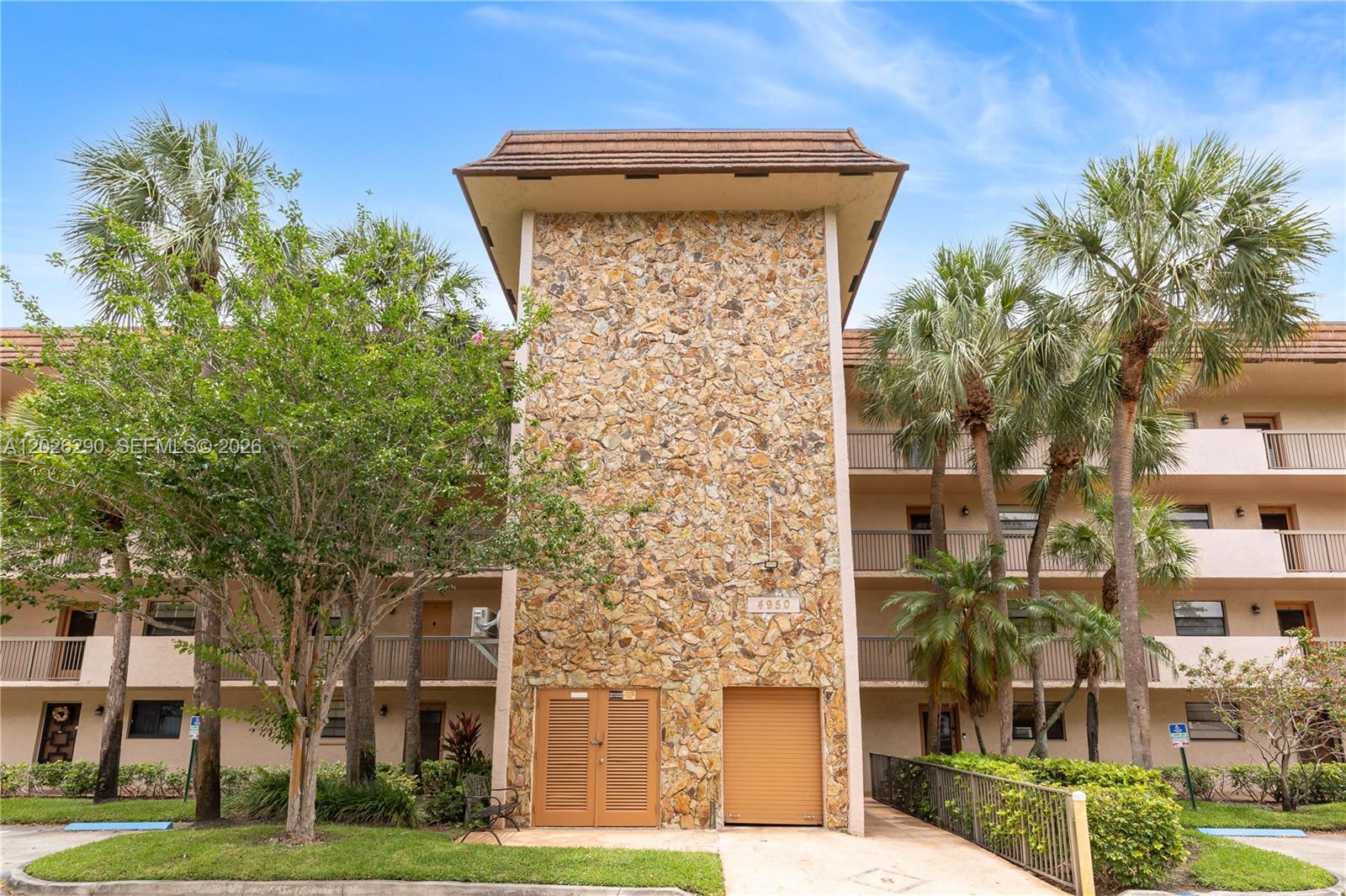 A multi-story apartment building features a central stone facade with a brown roof — 4950 E Sabal Palm Blvd # 106, Tamarac FL 33319, TAMARAC, FL
