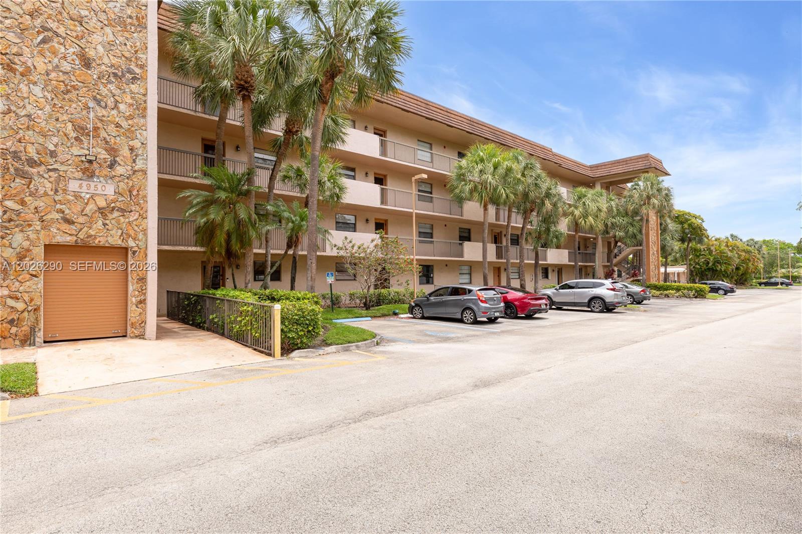 A multi-story apartment building features a stone facade, balconies, and a parking lot — 4950 E Sabal Palm Blvd # 106, Tamarac FL 33319, TAMARAC, FL