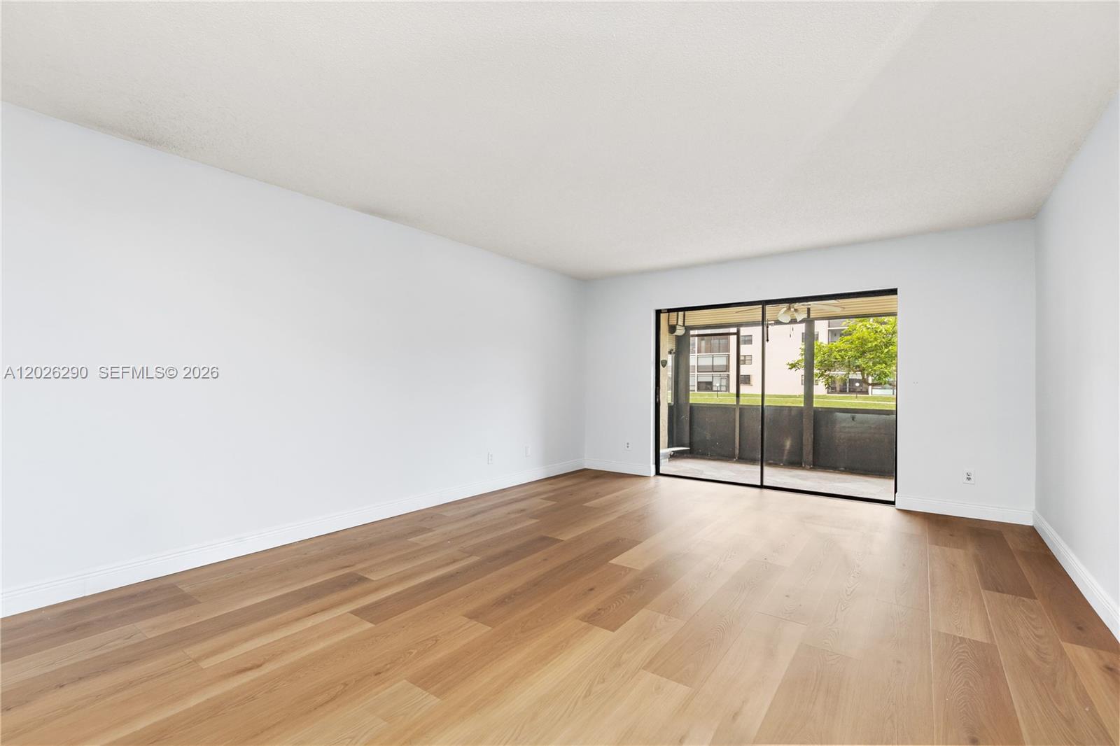 An empty room features light wood-look flooring, white walls, and a sliding glass door — 4950 E Sabal Palm Blvd # 106, Tamarac FL 33319, TAMARAC, FL