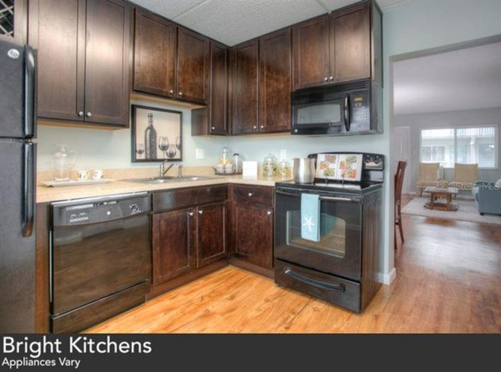 A kitchen with dark wood cabinets, black appliances, and light countertops over wood-look flooring — 1824 SHORE DRIVE S UNIT 205, SOUTH PASADENA, FL