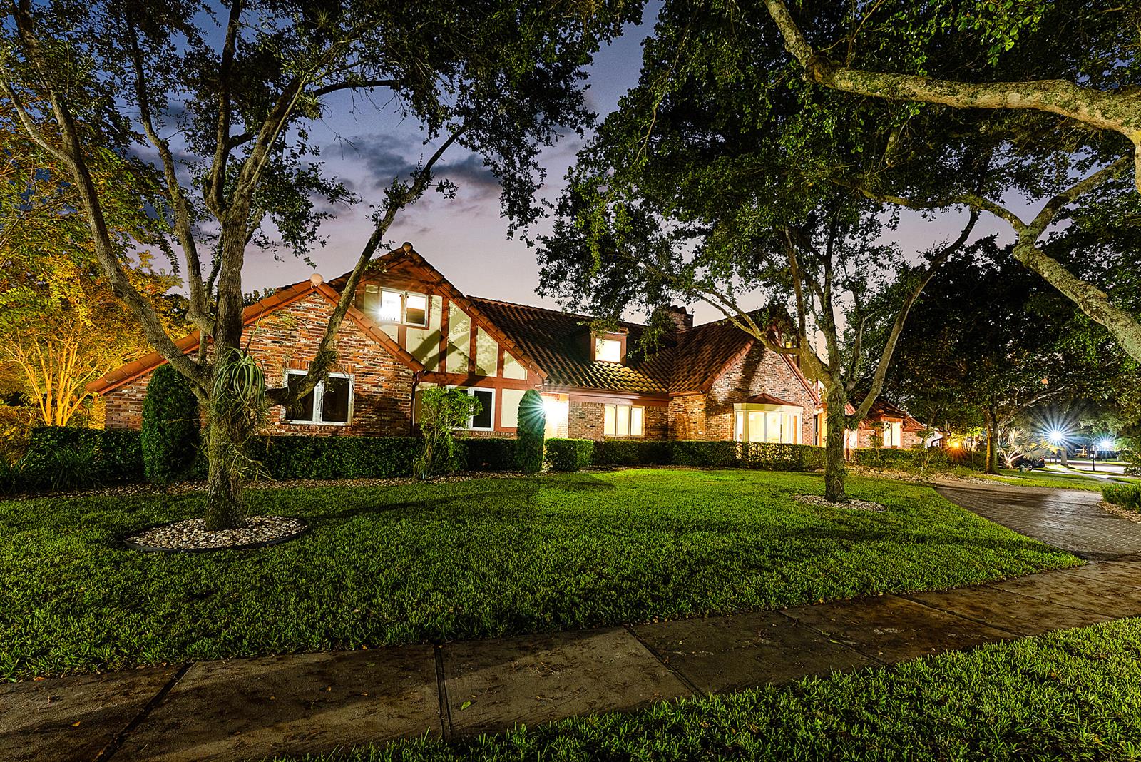 A brick Tudor-style house with a tile roof is illuminated at night behind a lawn — 3790 Kings Way, Boca Raton FL 33434, BOCA RATON, FL