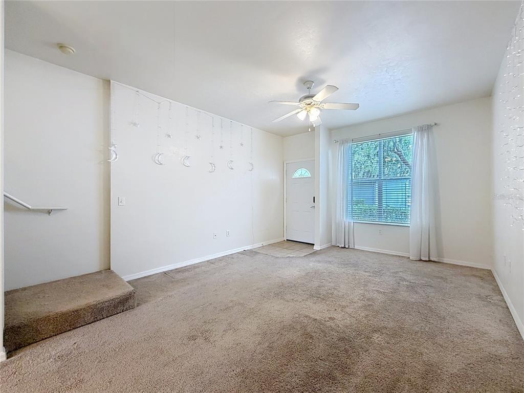 A carpeted living room features a ceiling fan, a front door, and a staircase landing — 3920 SW 20TH AVENUE UNIT 1306, GAINESVILLE, FL