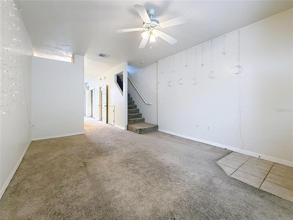 A carpeted living room features a ceiling fan, a staircase, and wall-mounted moon decorations — 3920 SW 20TH AVENUE UNIT 1306, GAINESVILLE, FL