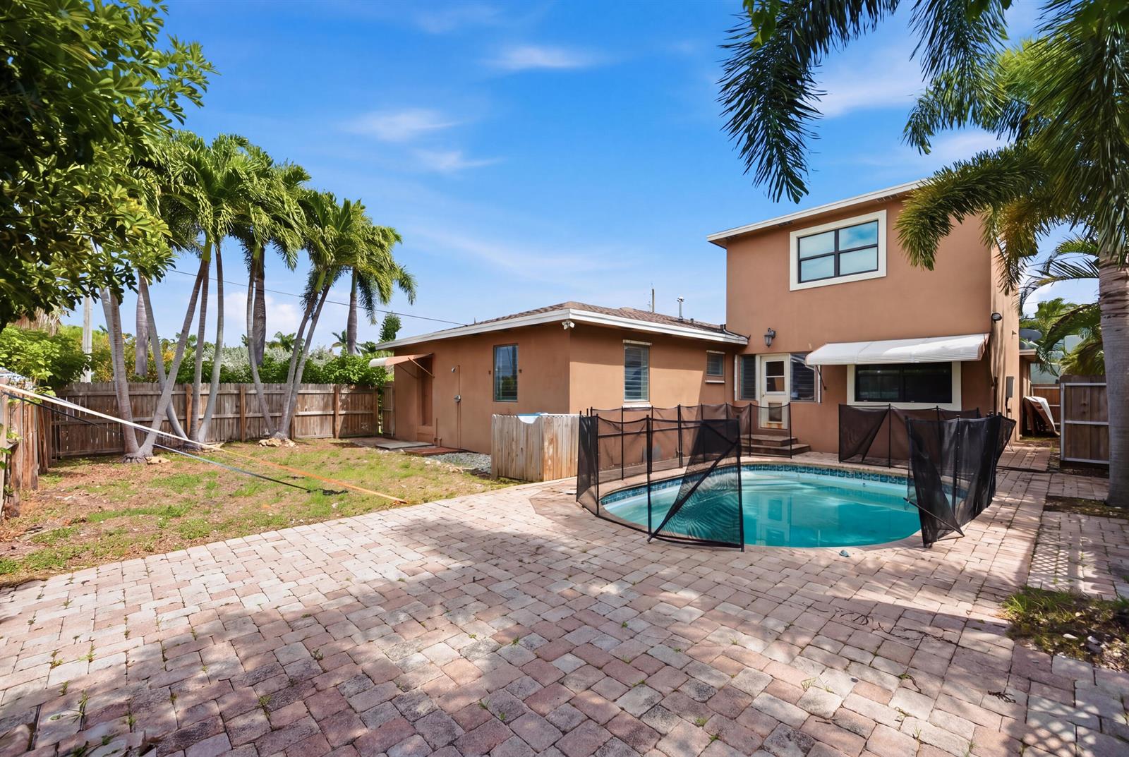 A backyard with a paved patio, a small swimming pool with a safety fence, and palms — 303 Cornell Drive, FL 33460, FL