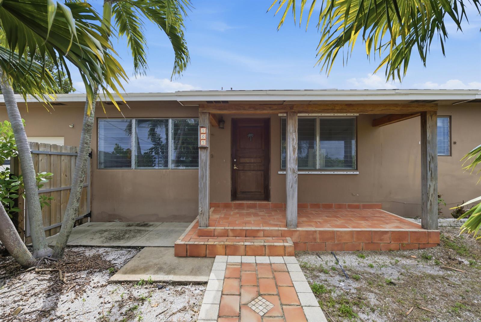 A single-story house exterior features a brown stucco facade, a tiled porch, and wooden posts — 303 Cornell Drive, FL 33460, FL