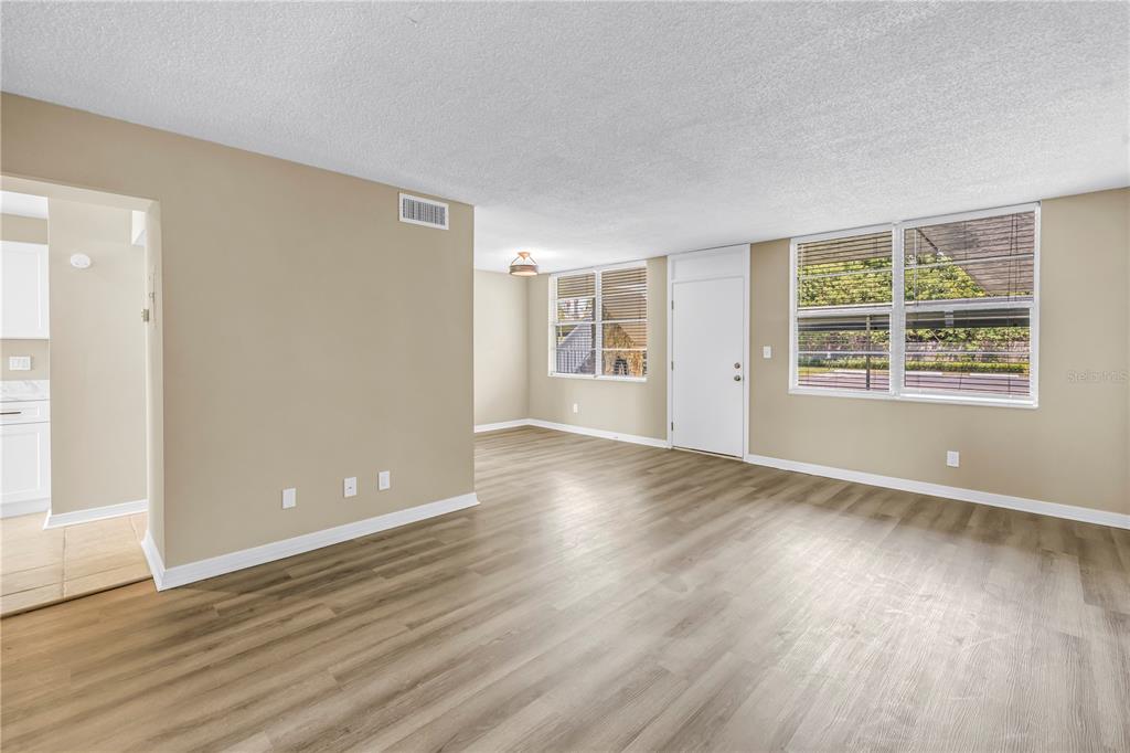 An empty living room with light-colored walls, wood-look flooring, and large windows — 4720 LOCUST STREET NE UNIT 116, ST PETERSBURG, FL