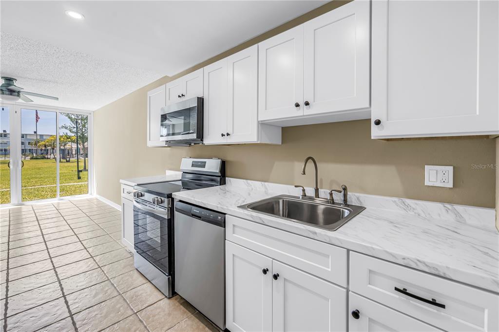 A kitchen with white cabinets, stainless steel appliances, and marble-look countertops overlooks a grassy area — 4720 LOCUST STREET NE UNIT 116, ST PETERSBURG, FL