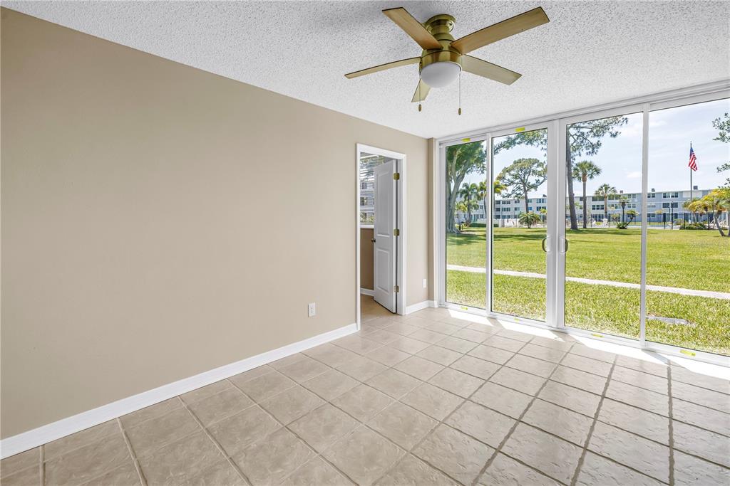 An empty room with beige walls, tile flooring, a ceiling fan, and sliding glass doors — 4720 LOCUST STREET NE UNIT 116, ST PETERSBURG, FL