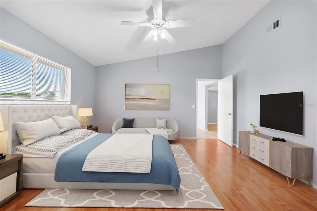A bedroom features a tufted headboard, a blue bedspread, a sofa, and a wall-mounted television — 7853 KENSINGHAM COURT, ORLANDO, FL