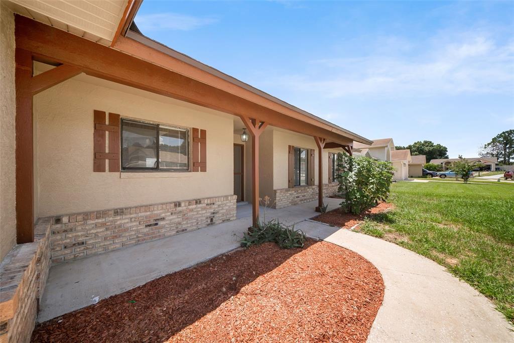 A covered front porch with a brick base and wooden support beams faces a lawn — 7853 KENSINGHAM COURT, ORLANDO, FL