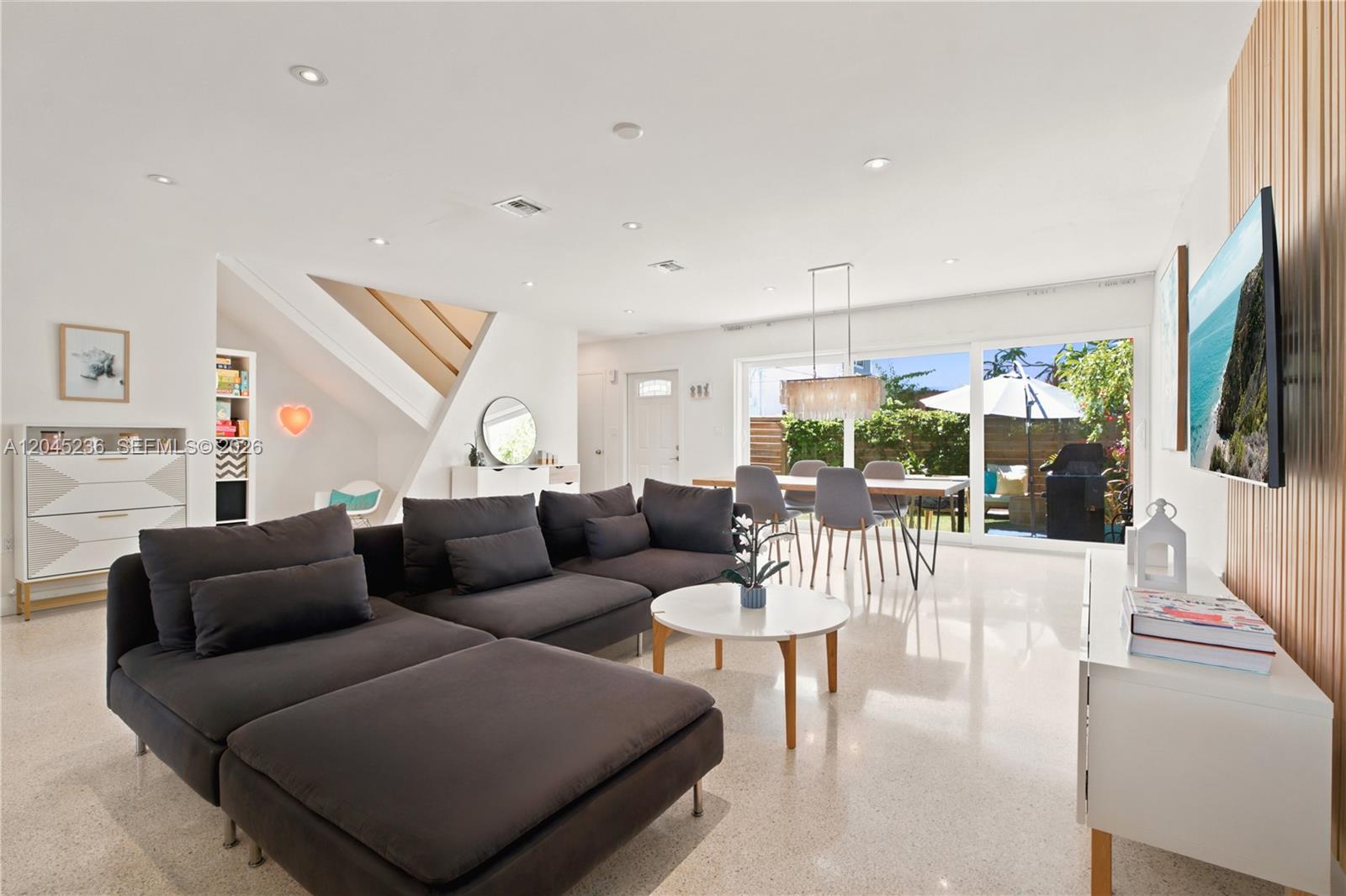 A modern living and dining area features a dark sectional sofa, white floors, and patio access — 7334 Gary Ave # 7334, Miami Beach FL 33141, MIAMI BEACH, FL