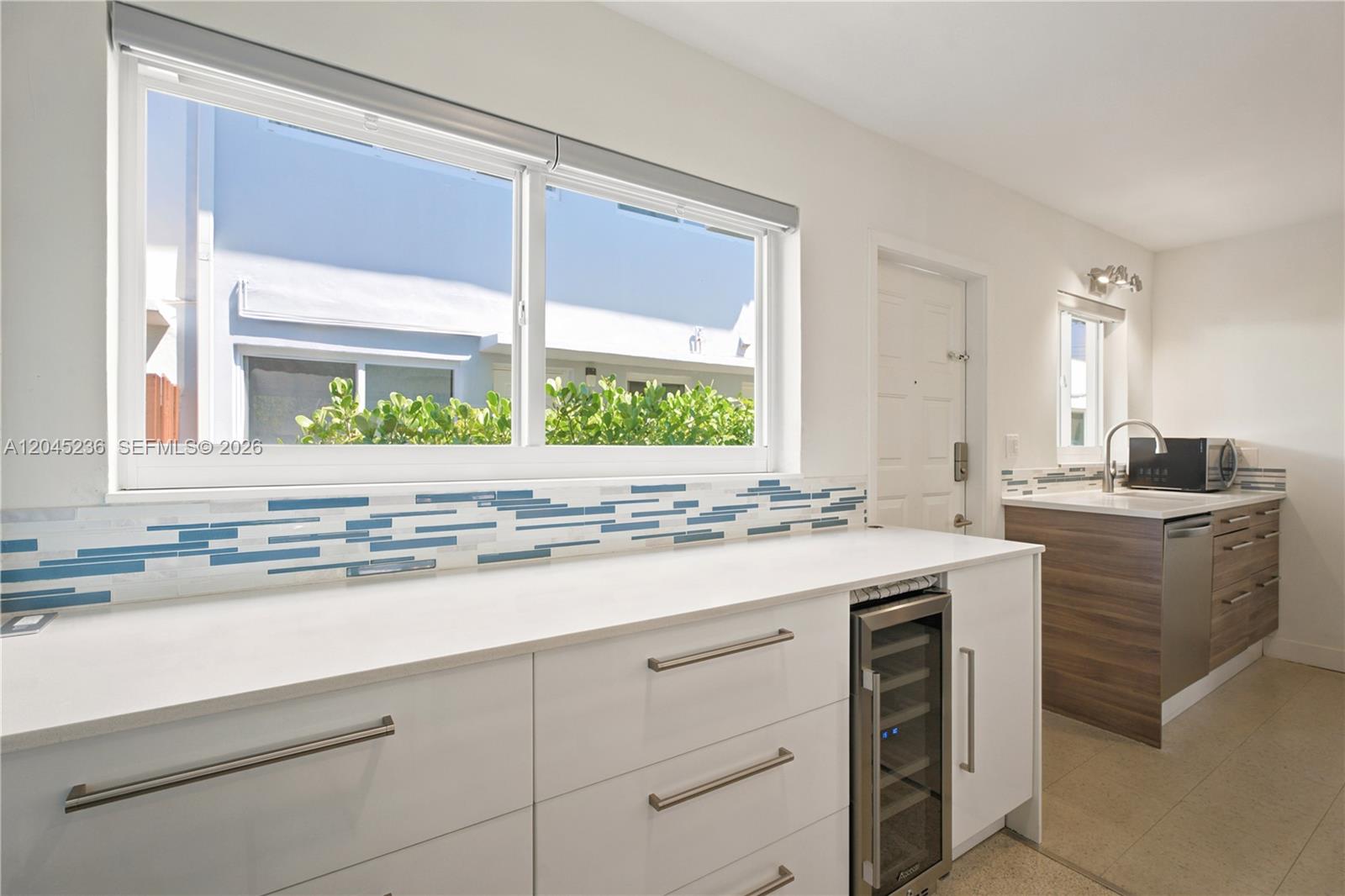 A kitchen features white cabinets, a wine cooler, and a blue-tiled backsplash under a window — 7334 Gary Ave # 7334, Miami Beach FL 33141, MIAMI BEACH, FL