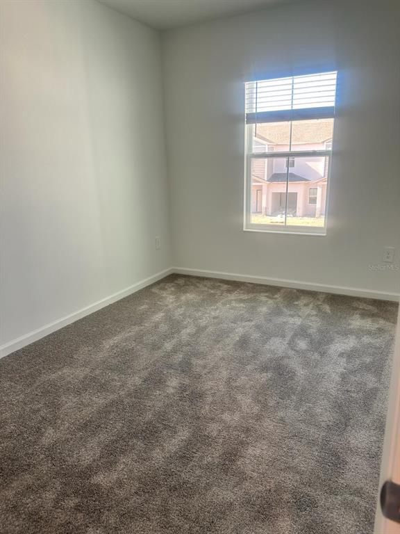 An empty bedroom features gray carpet, white walls, and a window overlooking a neighboring house — 3319 LAURENT LOOP UNIT 3319, DAVENPORT, FL