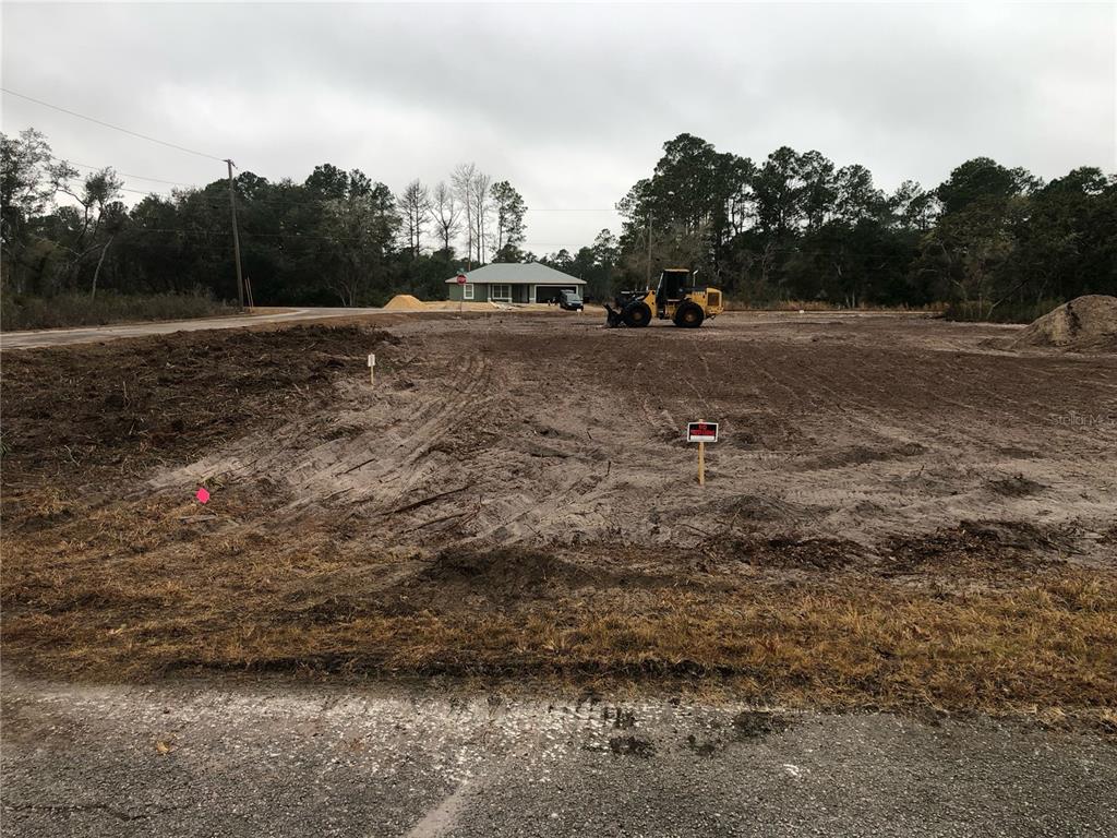 A cleared, vacant lot features a construction vehicle and a house in the background — 000 FISHER LOOP, OCKLAWAHA, FL