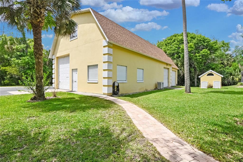A yellow two-story garage with a paver walkway and a small shed on the lawn — 1711 HIDEAWAY FOREST TRAIL, NEW SMYRNA BEACH, FL