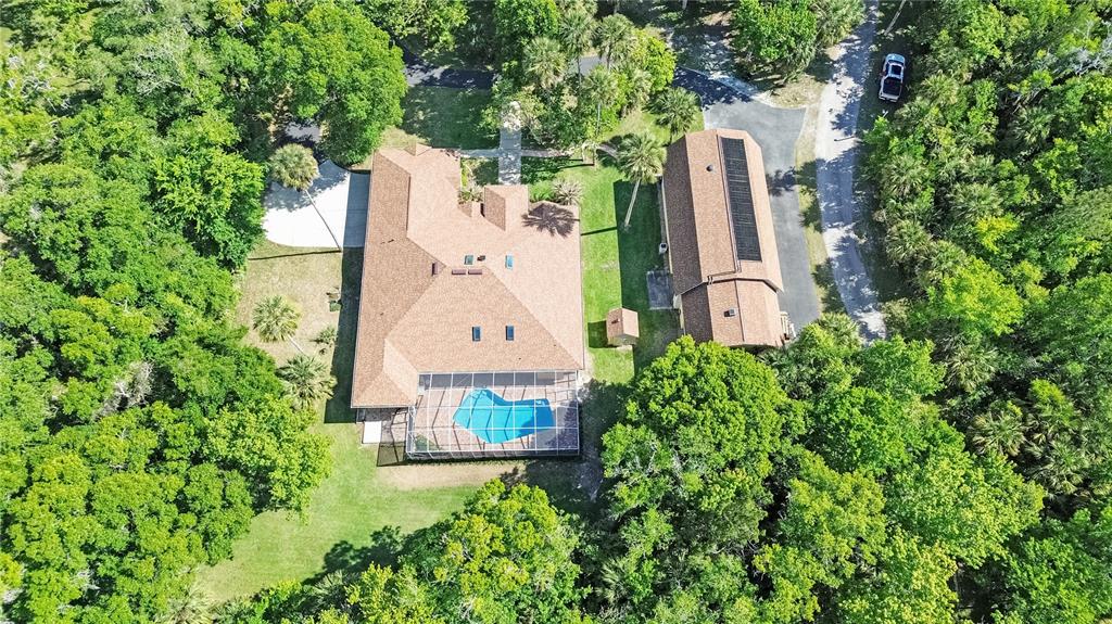 An aerial view shows a house with a pool enclosure, a detached garage, and trees — 1711 HIDEAWAY FOREST TRAIL, NEW SMYRNA BEACH, FL