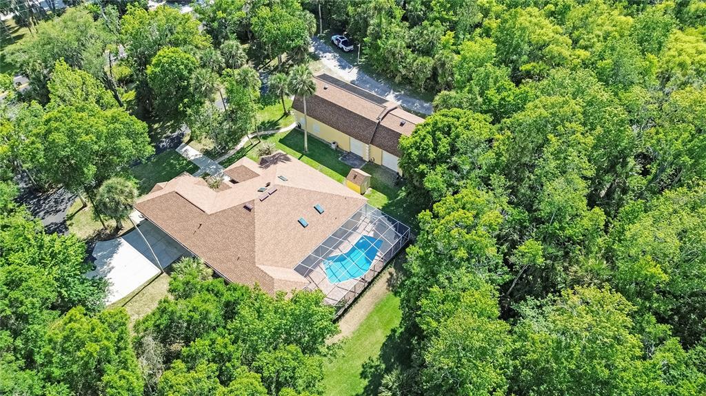 An aerial view shows a house with a pool enclosure, a detached garage, and surrounding trees — 1711 HIDEAWAY FOREST TRAIL, NEW SMYRNA BEACH, FL