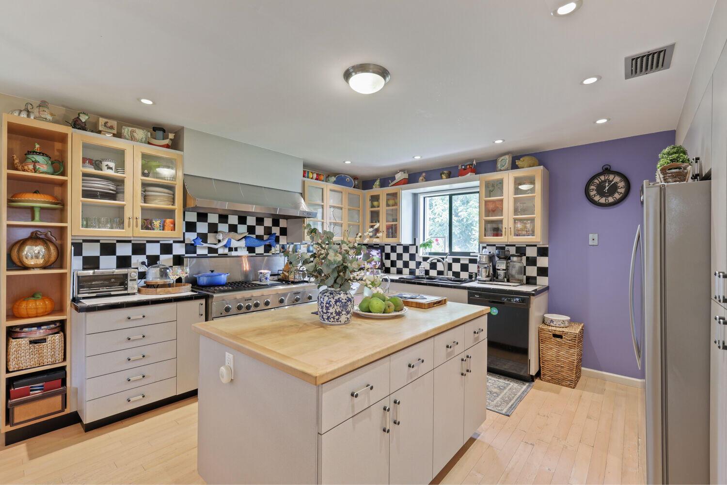 A kitchen features a central island, light wood floors, purple walls, and black-and-white checkered backsplash — 3918 Edgar Avenue, Boynton Beach FL 33436, BOYNTON BEACH, FL