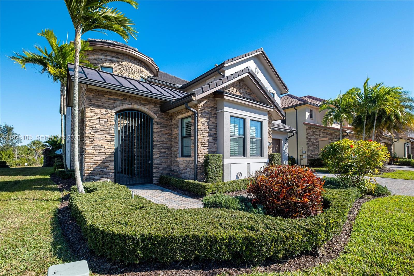 A stone-clad house features a gated entryway, a metal roof, and manicured landscaping — 11475 Watercrest Circle East, Parkland FL 33076, PARKLAND, FL