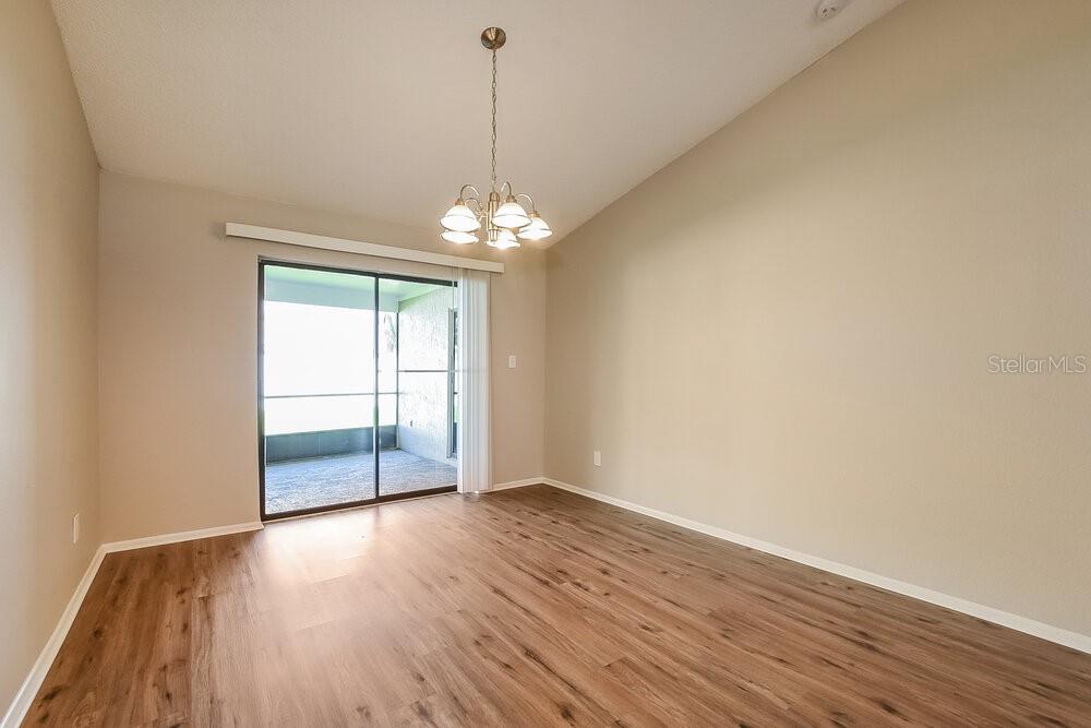 An empty dining room features wood-look flooring, a chandelier, and a sliding glass door — 1014 DISHMAN LOOP, OVIEDO, FL