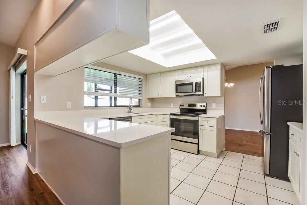 A kitchen with white cabinets, stainless steel appliances, a tile floor, and a large skylight — 1014 DISHMAN LOOP, OVIEDO, FL