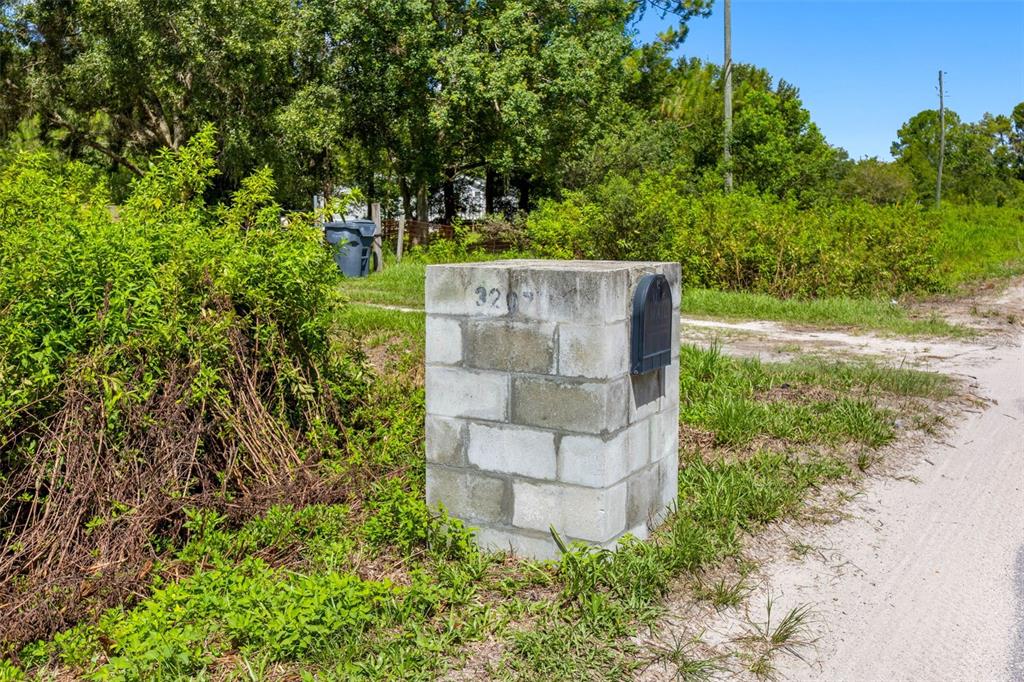 A concrete block mailbox structure stands beside a dirt road near dense green vegetation — 3207 CYPRESS TRAILS DRIVE, POLK CITY, FL